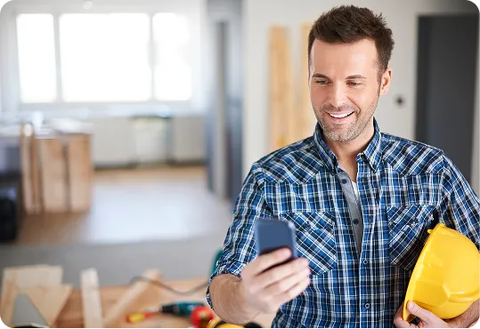 shows a person holding a yellow hard hat and using a smartphone.